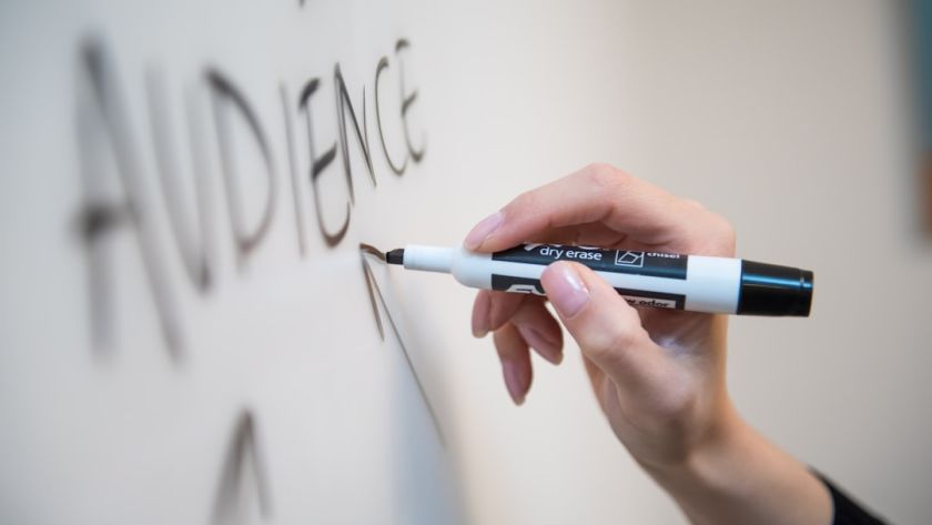 Woman's hand writing the word "audience" on a whiteboard, with arrows.