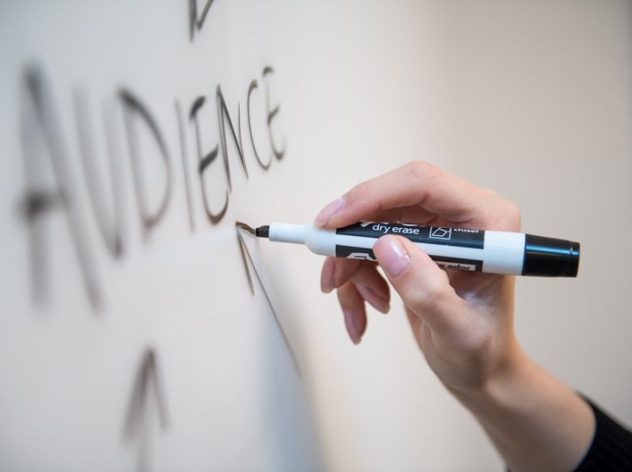 Woman's hand writing the word "audience" on a whiteboard, with arrows.