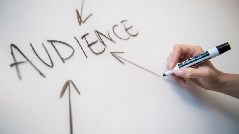 Woman's hand writing the word "audience" on a whiteboard, with arrows.