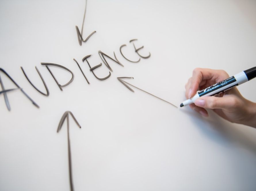 Woman's hand writing the word "audience" on a whiteboard, with arrows.